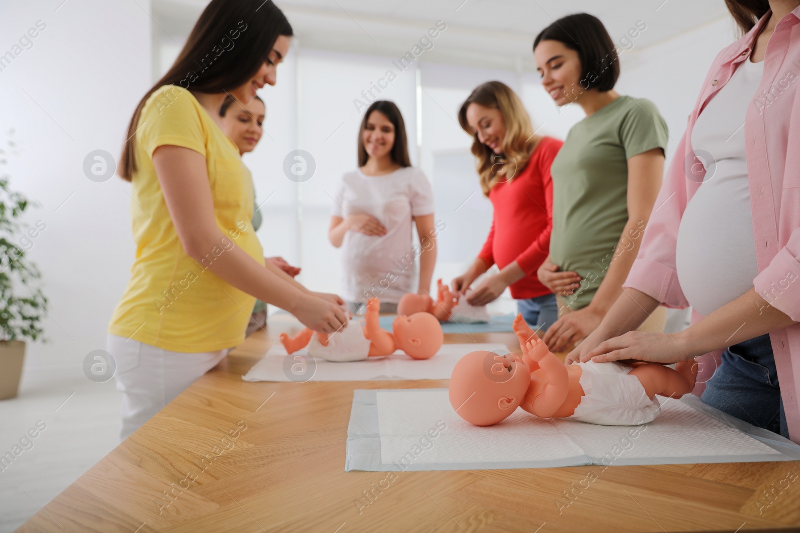 Photo of Pregnant women learning how to swaddle baby at courses for expectant mothers indoors, closeup