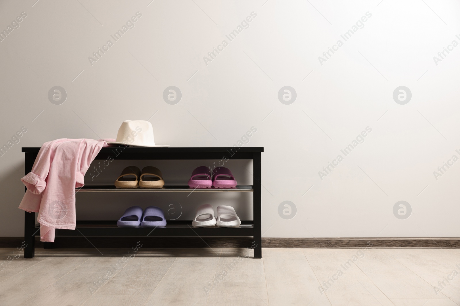 Photo of Storage bench with pairs of rubber slippers indoors. Space for text