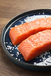 Fresh raw salmon with salt on wooden table, closeup