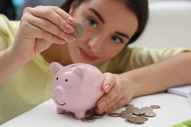 Woman putting coin into piggy bank at home, focus on hand. Money savings