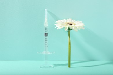 Cosmetology. Medical syringe and gerbera flower on turquoise background