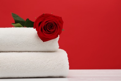 Photo of Soft clean towels with beautiful flower on table against color background. Space for text