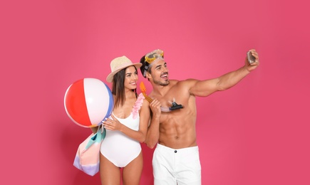 Photo of Young attractive couple in beachwear with snorkel and ball taking selfie on pink background