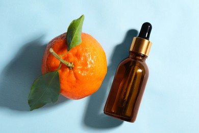 Photo of Aromatic tangerine essential oil in bottle and citrus fruit on light blue table, top view