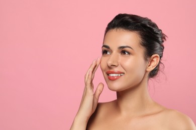 Photo of Woman applying cream under eyes on pink background, space for text. Skin care