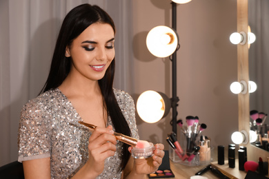 Beautiful young woman applying makeup near mirror in dressing room