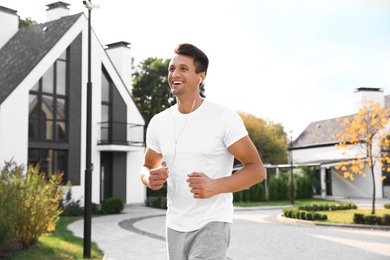 Photo of Young man with earphones running outdoors on sunny morning. Healthy lifestyle