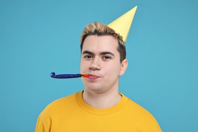 Photo of Young man with party hat and blower on light blue background