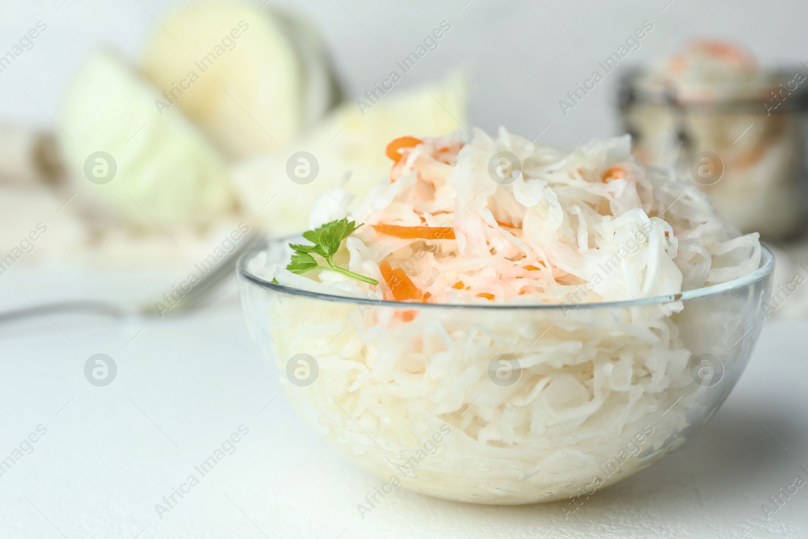 Photo of Glass bowl of tasty fermented cabbage on white table, closeup