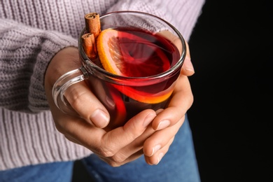 Photo of Woman holding cup with hot mulled wine against dark background, closeup
