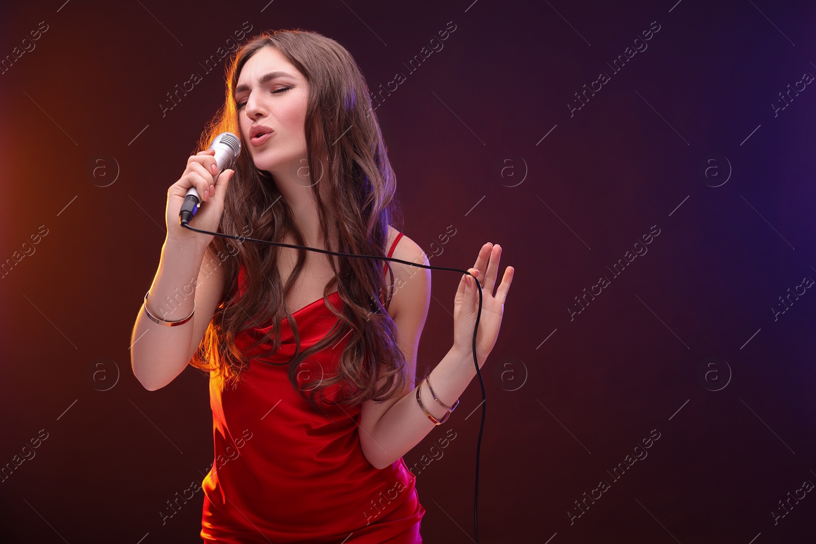 Photo of Emotional woman with microphone singing in color lights. Space for text