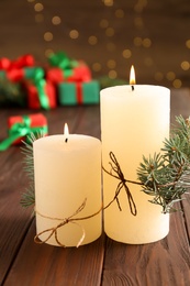 Photo of Burning candles with fir branches on wooden table against blurred background