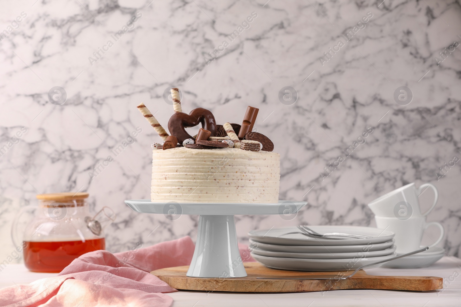 Photo of Delicious cake decorated with sweets and tableware on white table