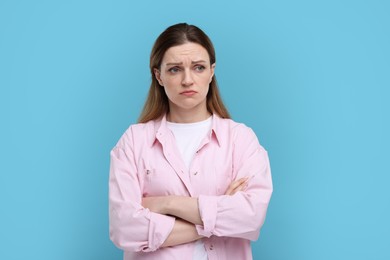 Portrait of sad woman with crossed arms on light blue background