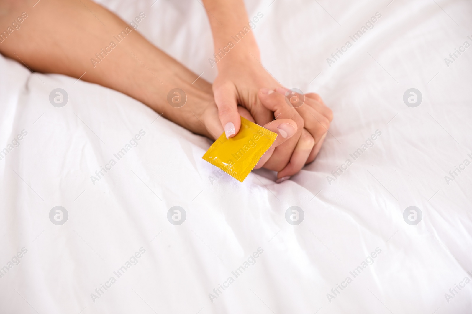 Photo of Woman and man holding condom together on bed, closeup. Safe sex concept