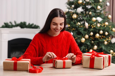 Photo of Happy woman decorating Christmas gift box at wooden table in room