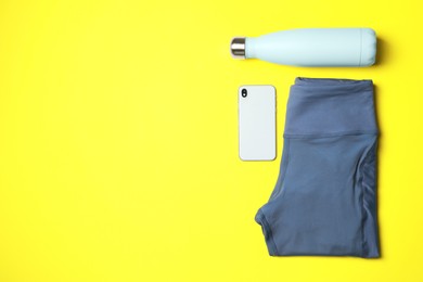 Photo of Stylish sports leggings, thermo bottle and smartphone on yellow background, flat lay. Space for text