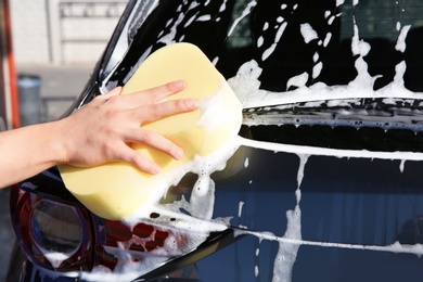 Worker cleaning automobile with sponge at car wash, closeup