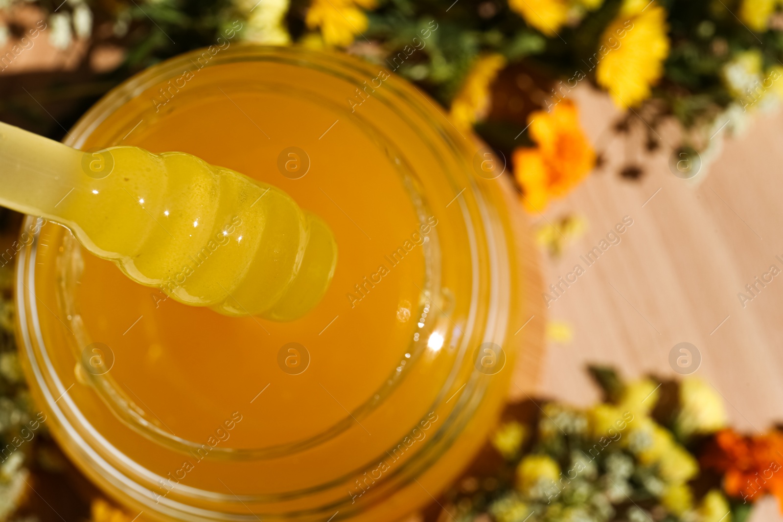 Photo of Taking delicious fresh honey with dipper from glass on wooden table, closeup