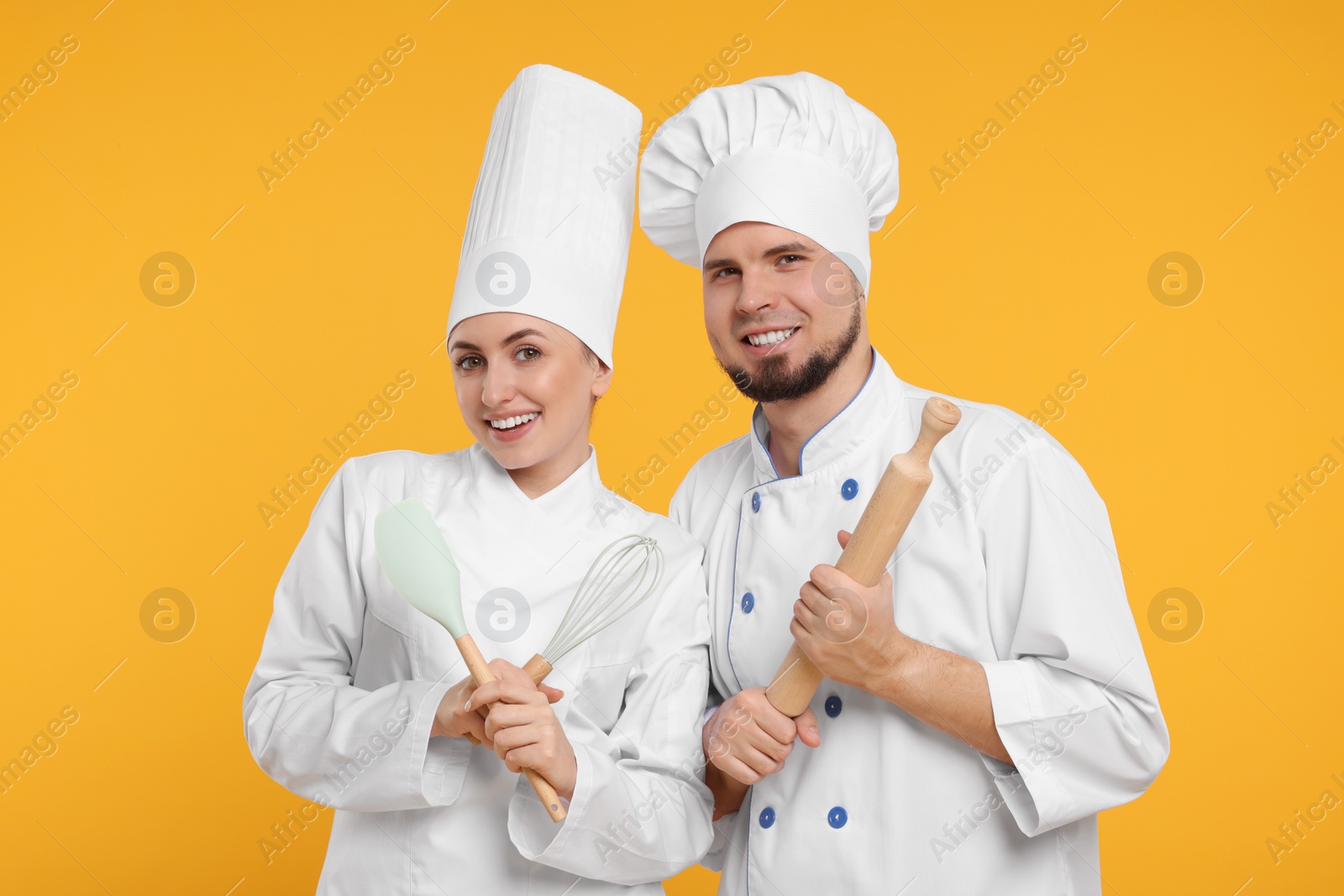 Photo of Happy confectioners in uniforms holding professional tools on yellow background