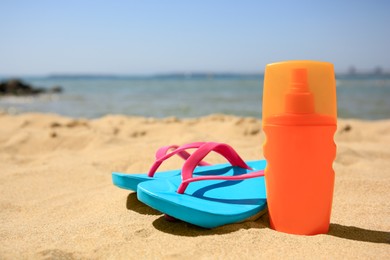 Photo of Sunscreen and flip flops on sandy beach, space for text. Sun protection care