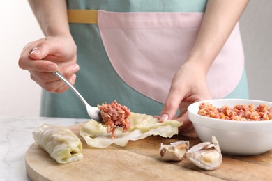 Woman preparing stuffed cabbage roll at white marble table, closeup