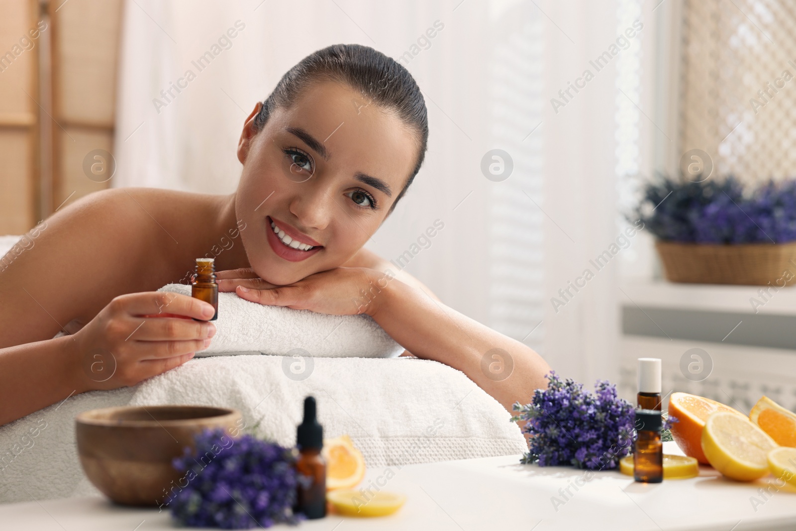 Photo of Beautiful young woman with bottle of essential oil on massage couch in spa salon