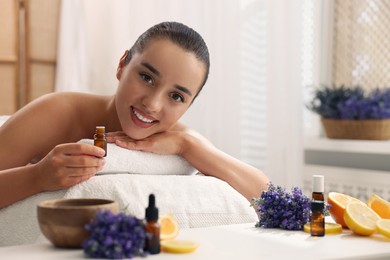 Photo of Beautiful young woman with bottle of essential oil on massage couch in spa salon