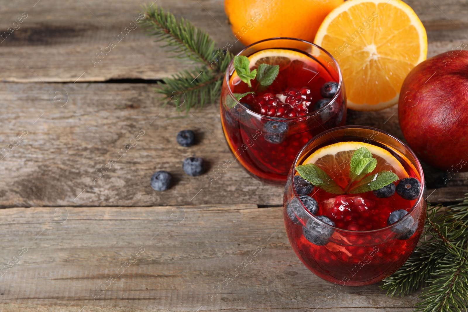 Photo of Aromatic Christmas Sangria drink in glasses, fir branches and ingredients on wooden table. Space for text