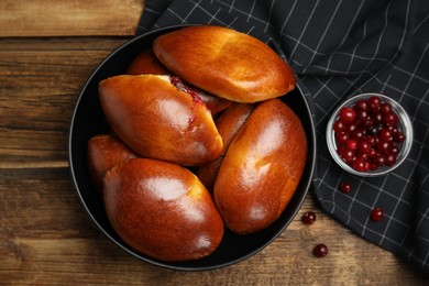 Photo of Delicious baked cranberry pirozhki in bowl on wooden table, flat lay