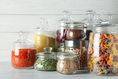 Glass jars with different types of groats and pasta on white wooden table