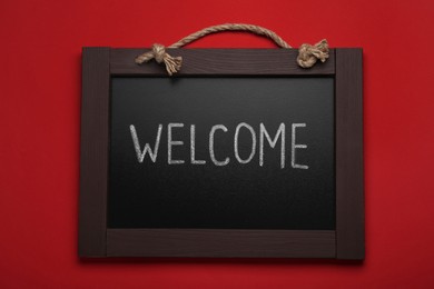 Photo of Small chalkboard with word Welcome on red background, top view
