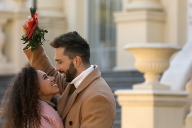 Happy couple under mistletoe bunch outdoors. Space for text