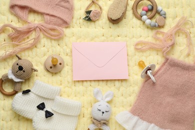 Baby shower party. Envelope surrounded by stuff for child on yellow knitted fabric, flat lay