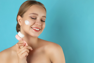 Photo of Young woman washing face with brush and cleansing foam on light blue background. Cosmetic products
