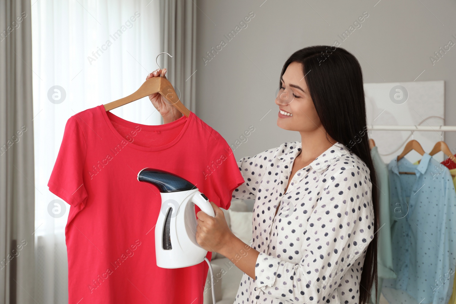 Photo of Woman steaming t-shirt on hanger at home