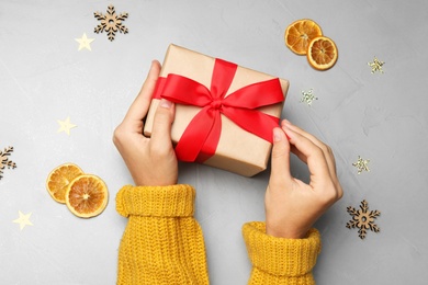 Young woman holding Christmas gift on grey stone background, flat lay