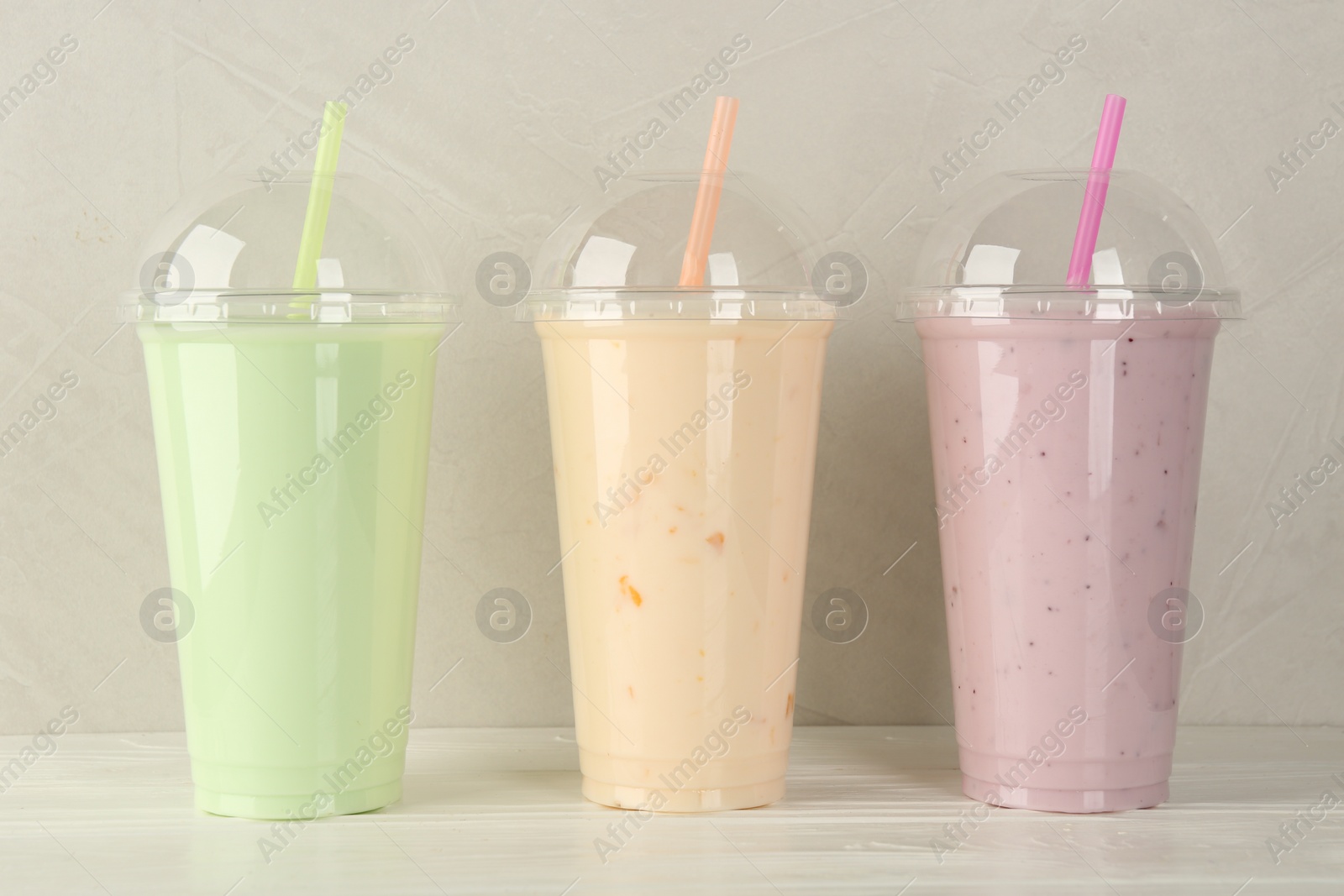 Photo of Plastic cups of different tasty smoothie on white wooden table