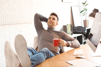 Photo of Young man with cup of drink relaxing at table in office during break