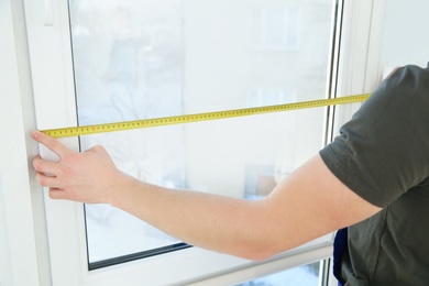 Photo of Service man measuring window for installation indoors, closeup