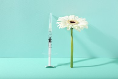 Photo of Cosmetology. Medical syringe and gerbera flower on turquoise background