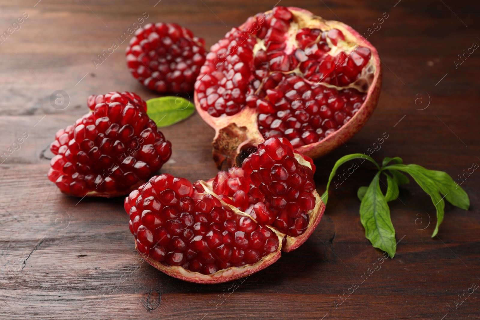 Photo of Cut fresh pomegranate and green leaves on wooden table, closeup