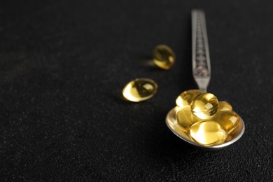 Photo of Spoon with cod liver oil pills and space for text on dark background, closeup