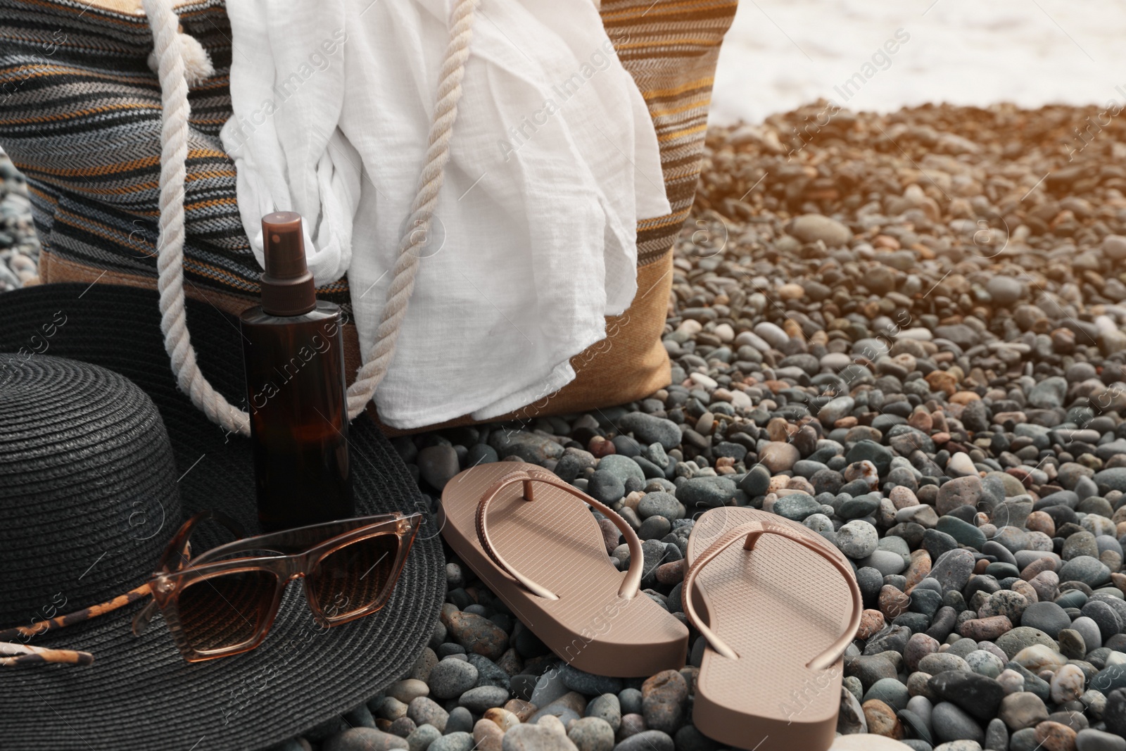 Photo of Beautiful hat with sunglasses, bag and flip flops near sea on pebble beach