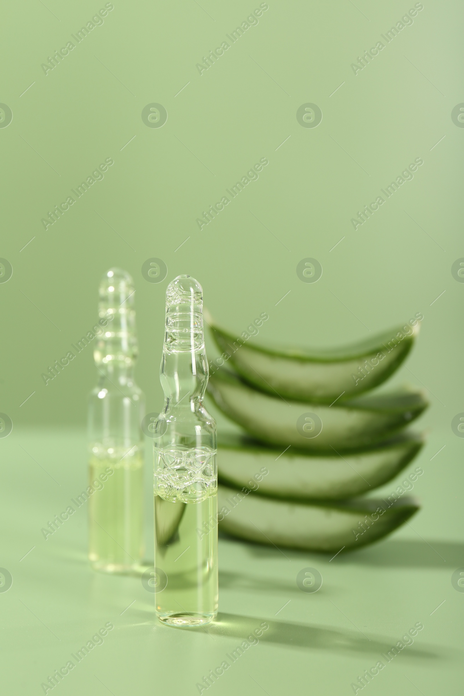 Photo of Skincare ampoules with extract of aloe vera and cut leaves on pale green background