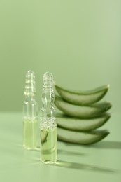 Skincare ampoules with extract of aloe vera and cut leaves on pale green background