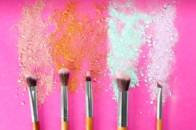 Photo of Makeup brushes and scattered eye shadows on bright pink background, flat lay