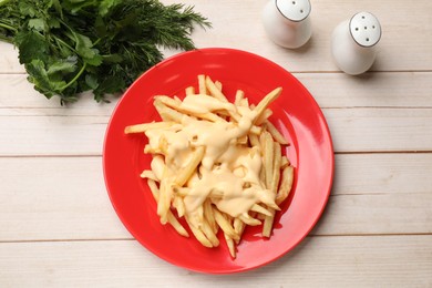 Photo of Delicious french fries with cheese sauce, greens and spice shakers on wooden table, flat lay