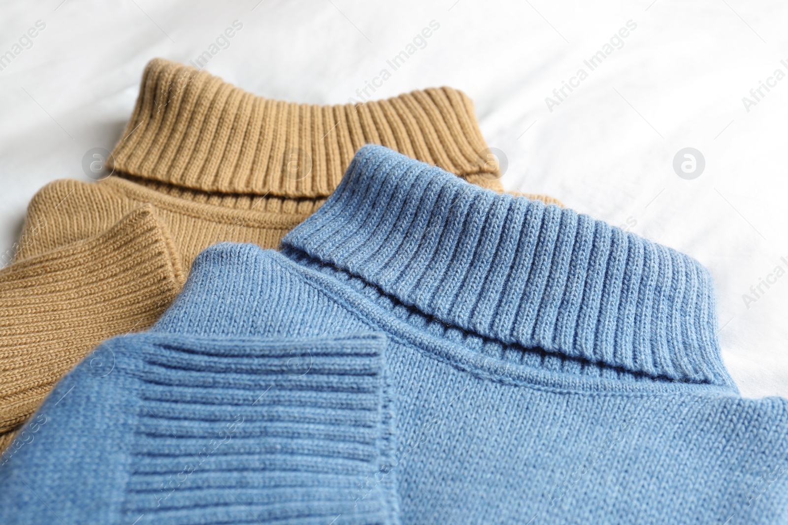 Photo of Stylish knitted sweaters on white fabric, closeup