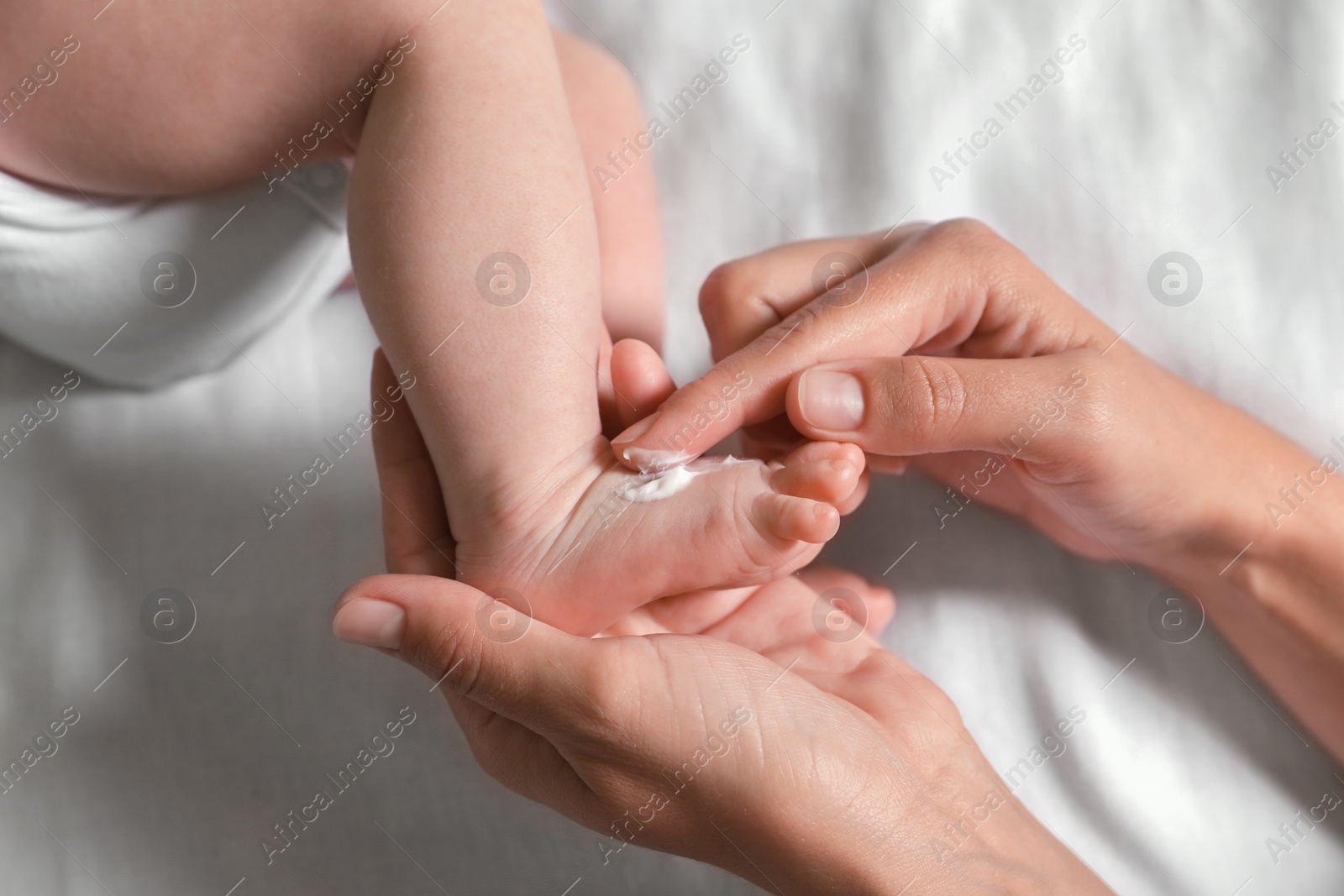 Photo of Mother applying moisturizing cream onto baby`s foot on bed, top view